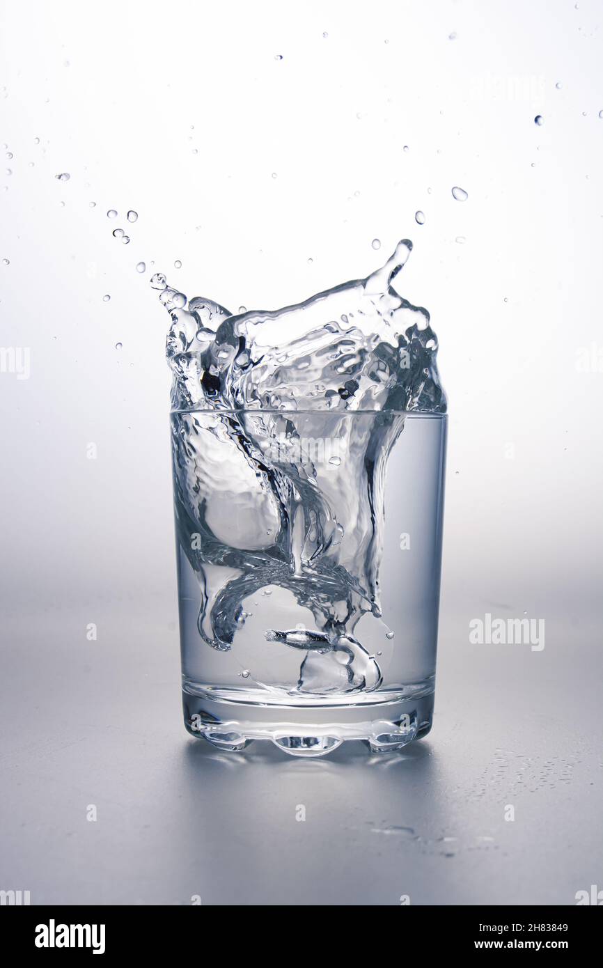 Bicchiere d'acqua con spruzzi su superficie grigio chiaro e sfondo bianco. Foto Stock