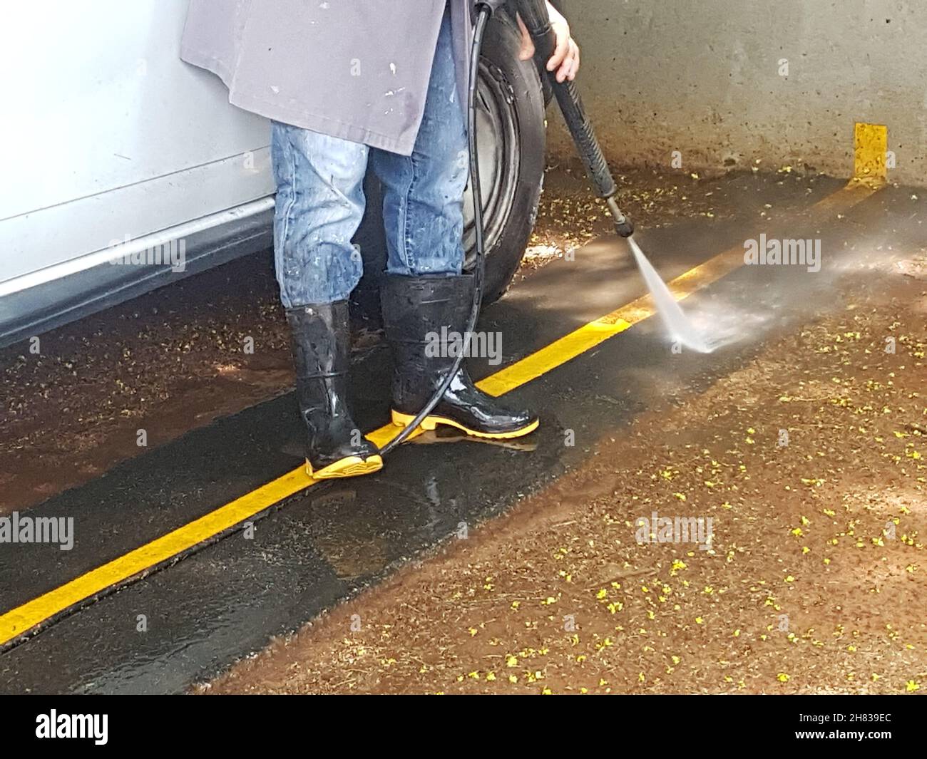 Stivali in gomma, piedi per uomo protetti quando si lava il pavimento con la macchina. Foto Stock