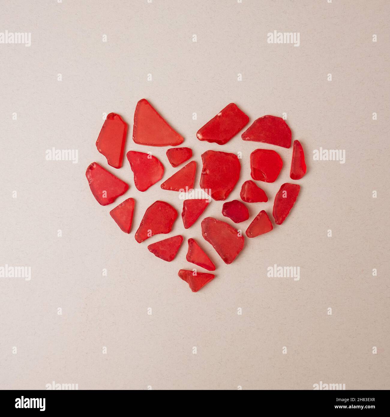 Simbolo del cuore fatto di pezzi di vetro rosso rotto su sfondo beige. Concetto minimo Heartbreak. Foto Stock