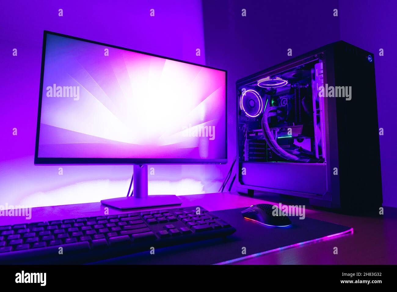 Moderno computer per videogiochi con display, custodia di raffreddamento ad acqua, tastiera, mouse su tappetino per giochi. Luce LED viola sullo sfondo Foto Stock