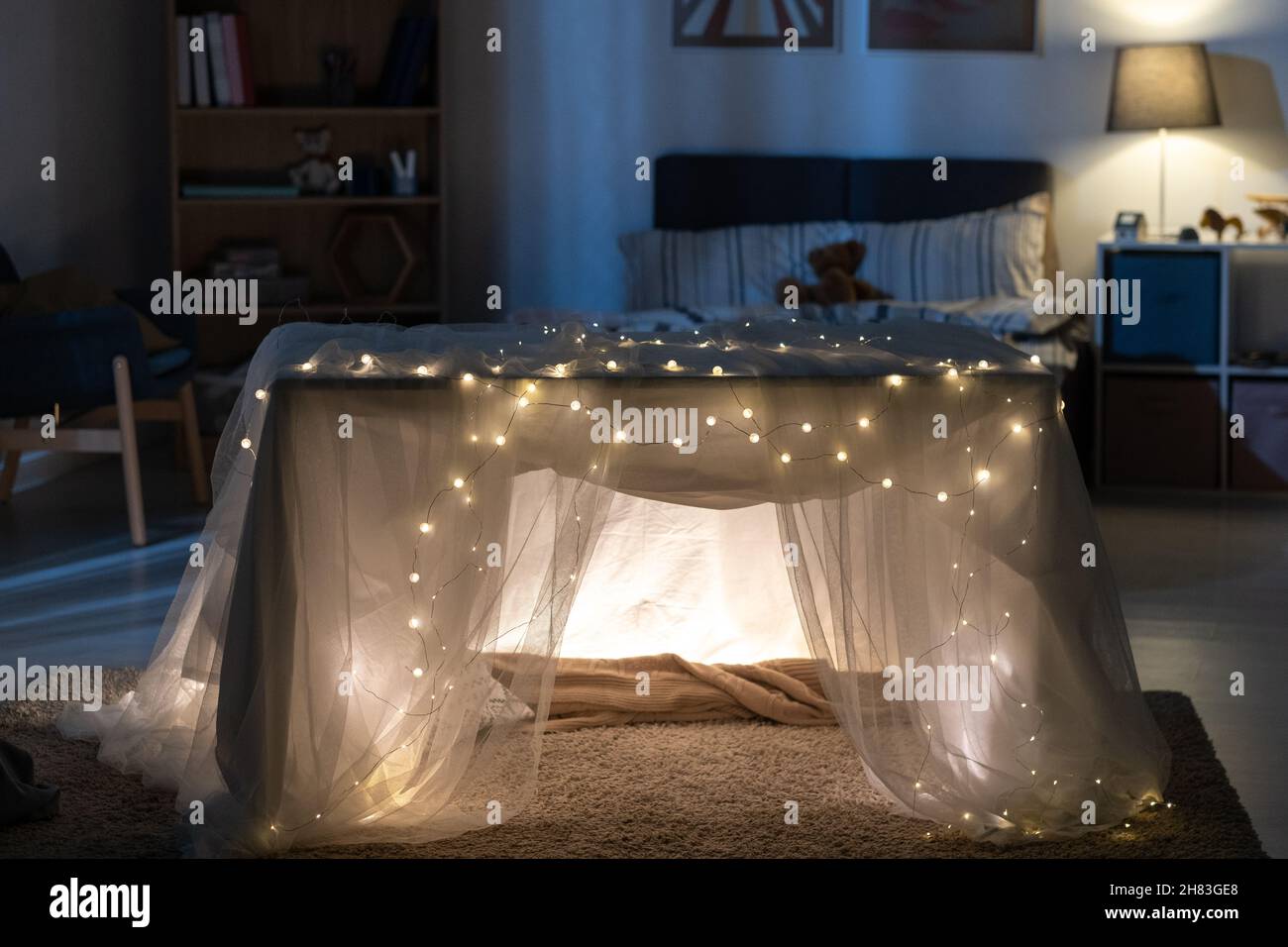 Accogliente tenda da gioco fatta a mano decorata con tulle e luci di Natale in camera asilo scuro Foto Stock
