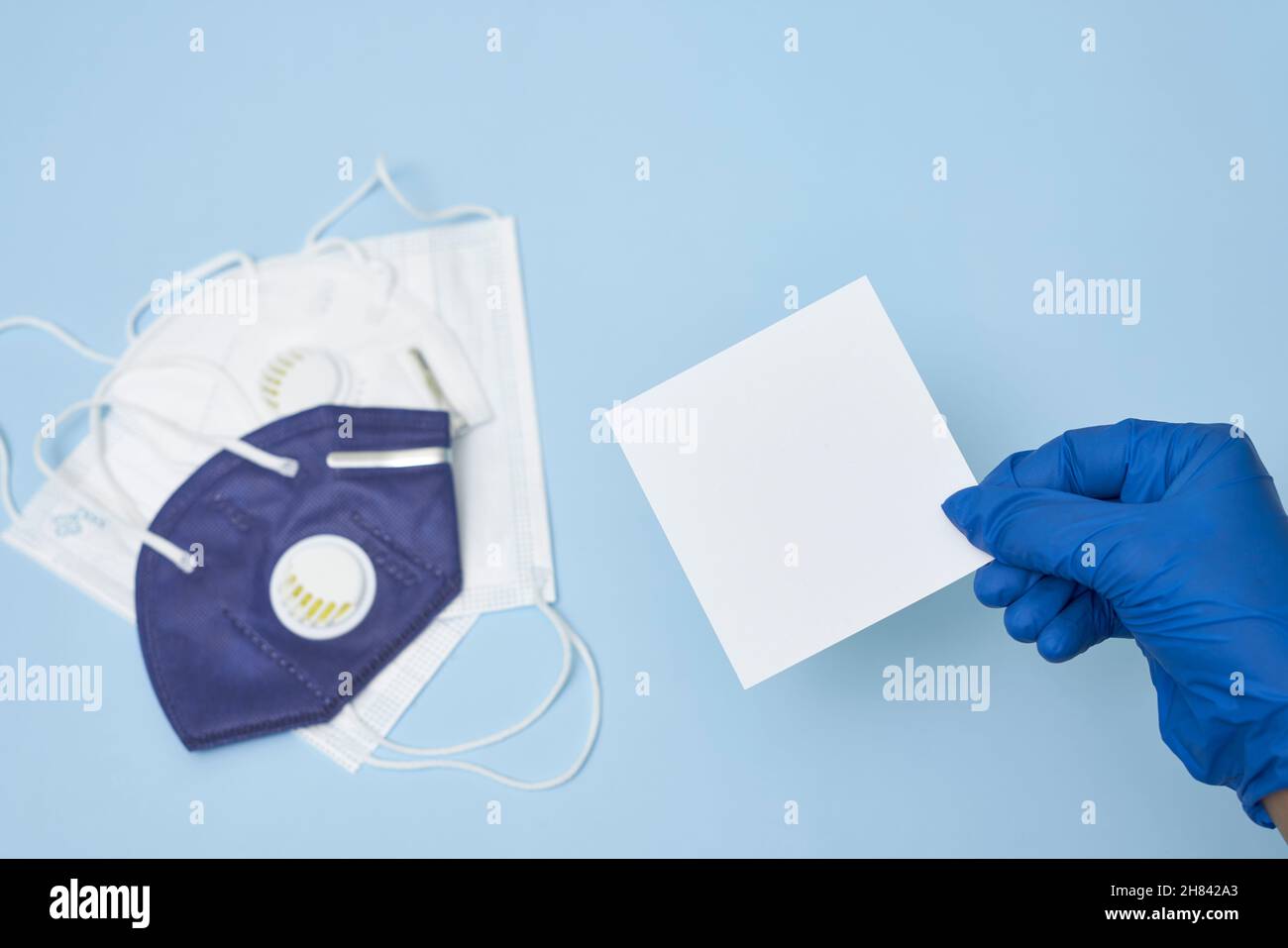 La mano del medico tiene una scheda bianca sopra un mucchio delle maschere di faccia. Spazio di copia Foto Stock