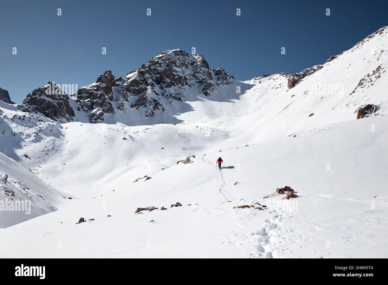 Uomo con zaino che cammina sulla collina della neve nelle belle montagne contro il cielo blu in Almaty, Kazakhstan Foto Stock