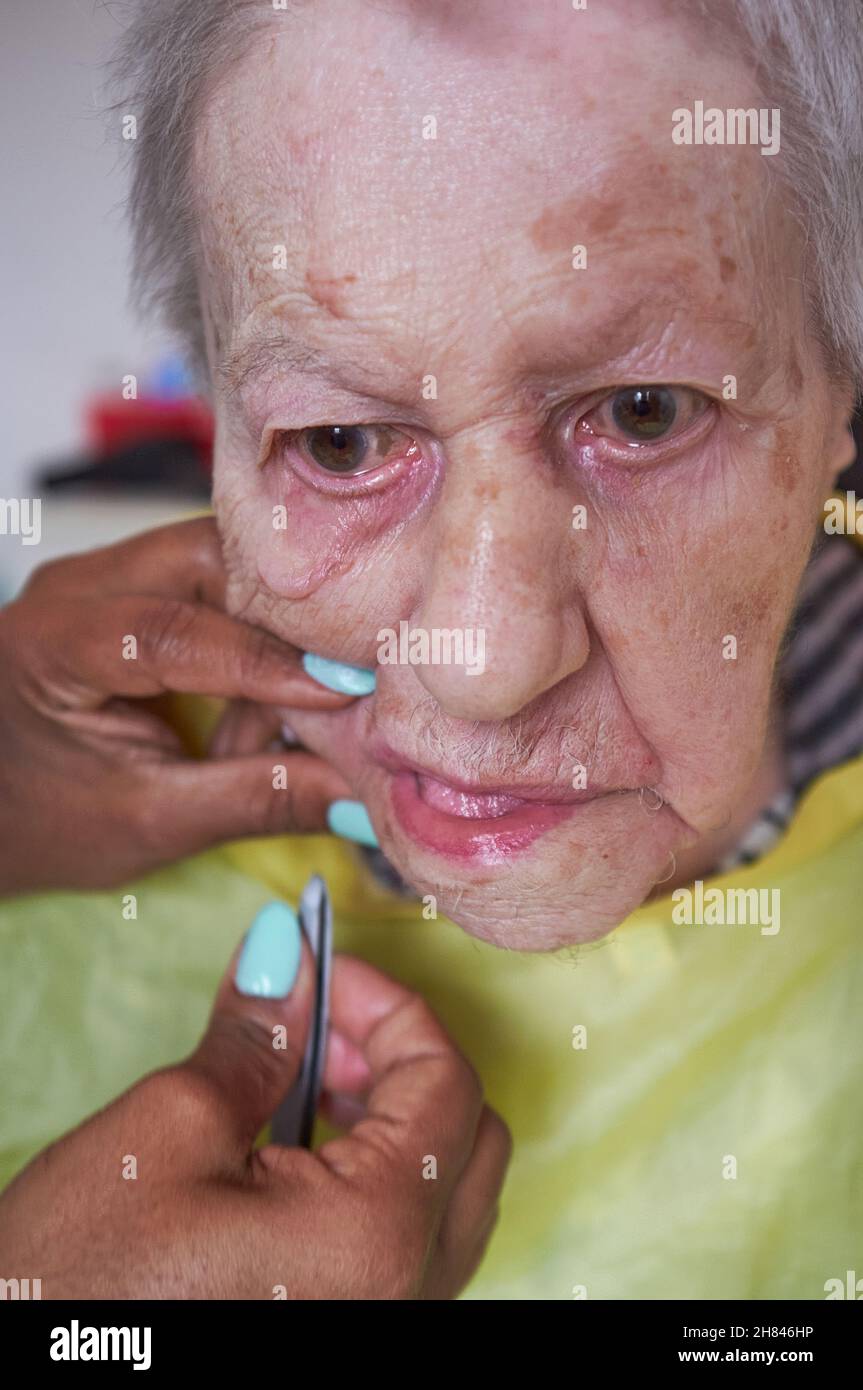 donna anziana che riceve la rimozione dei capelli del viso da un operatore sanitario afroamericano Foto Stock