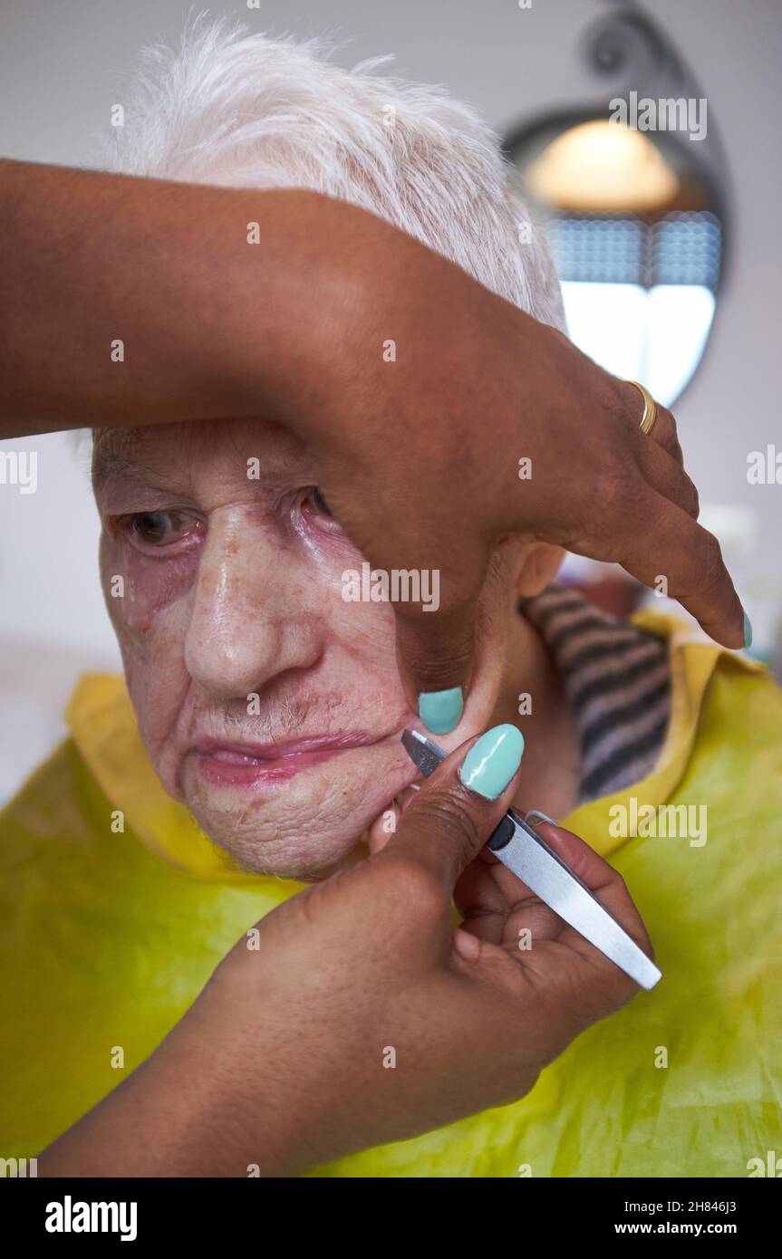 donna anziana che riceve la rimozione dei capelli del viso da un operatore sanitario afroamericano Foto Stock