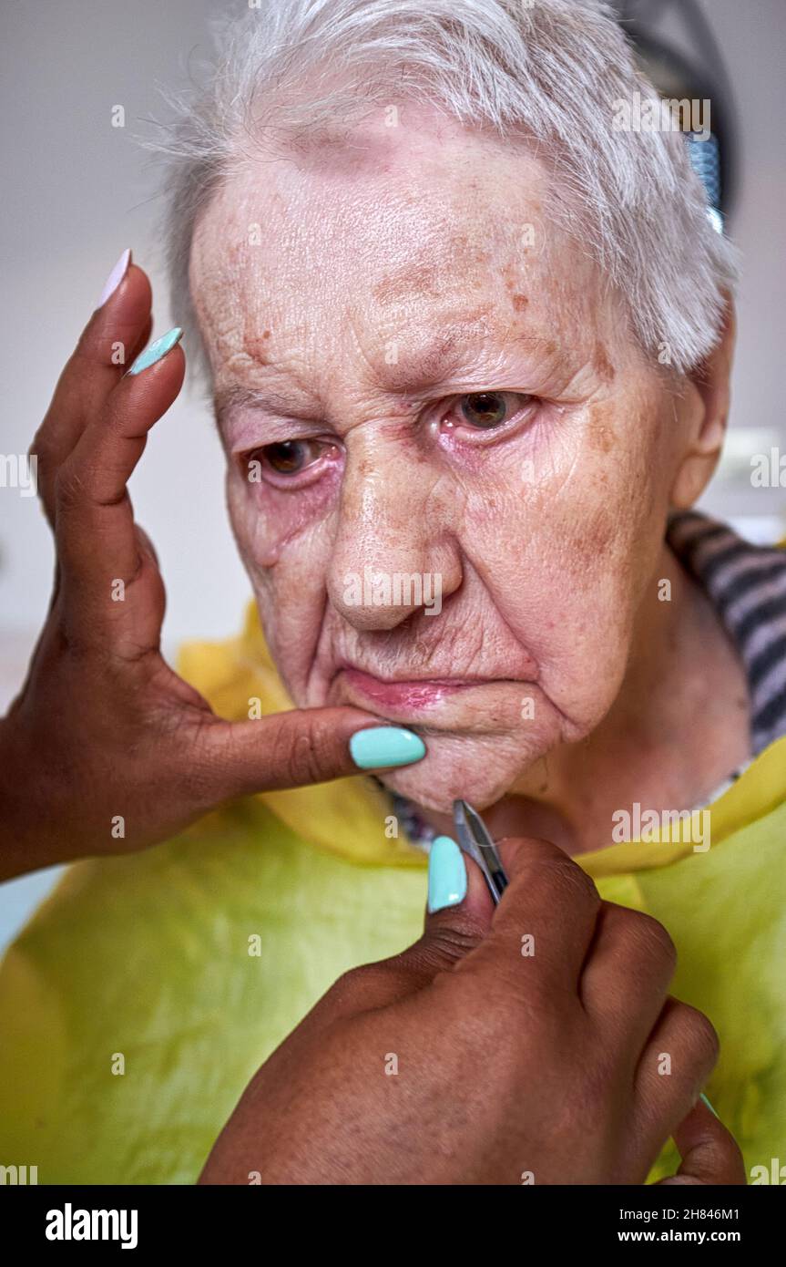 donna anziana che riceve la rimozione dei capelli del viso da un operatore sanitario afroamericano Foto Stock