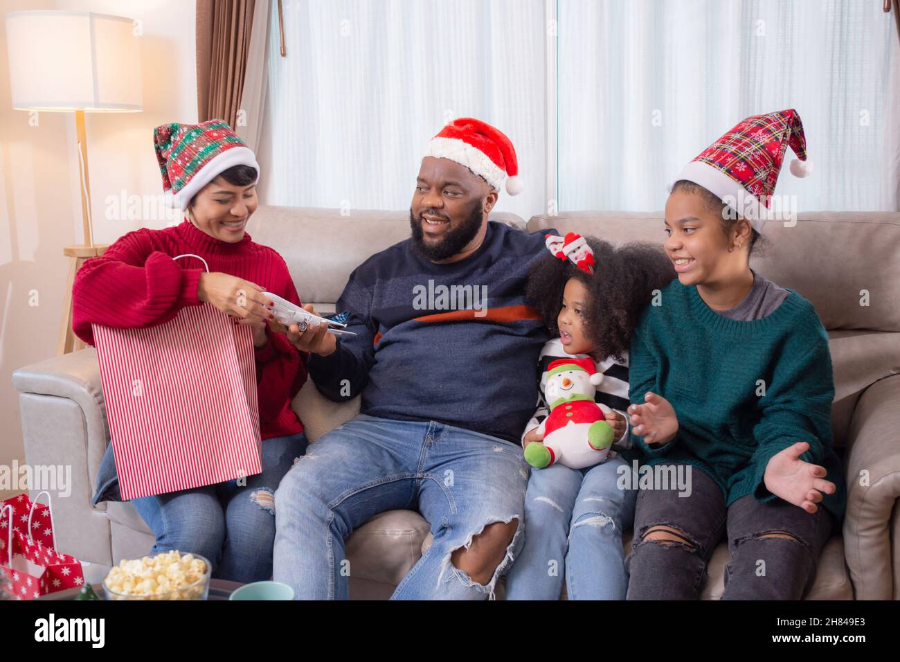 Felice mamma africana di famiglia che dà una borsa di shopping in regalo per la celebrazione con papà e figlia insieme per sorpresa nel soggiorno a casa a Chris Foto Stock