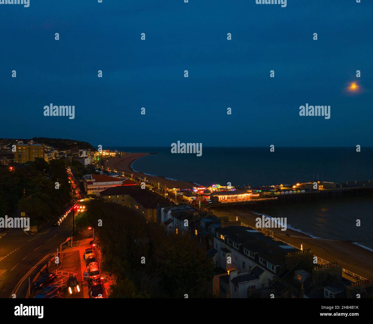 Una fotografia aerea di Hastings, Sussex, UK, Inghilterra, scattata in un'ora blu con il molo illuminato e che si aggetta in mare. Foto Stock