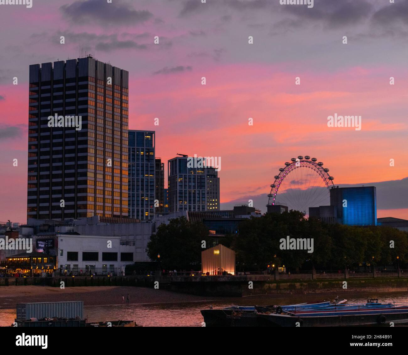 Un luminoso tramonto arancione e rosa sul tamigi girato dal lato nord, mostrando la riva sud, il teatro nazionale e l'occhio di Londra. Foto Stock