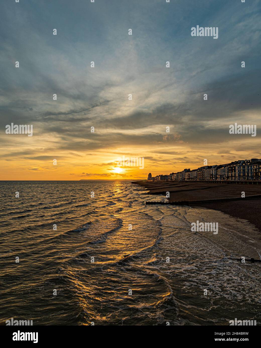 Tramonto e ora d'oro su Hastings Pier, Inghilterra, Regno Unito guardando verso Eastbourne con il mare e le grotte in primo piano. Promenade Foto Stock