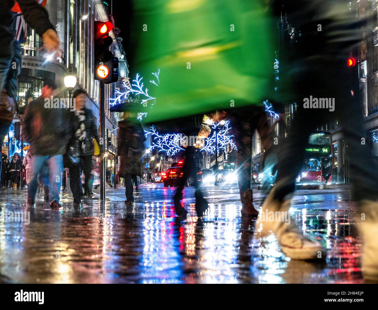 Gli acquirenti di Natale si piovono riflessi scena di traffico piovoso marciapiede e ombrelloni in una pioggia spazzata Regent Street con luci di Natale dietro Londra UK Foto Stock
