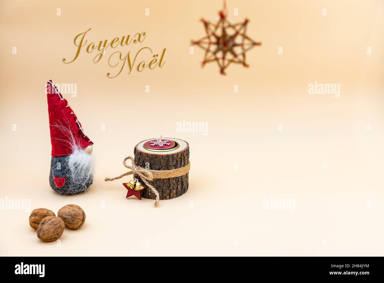 Cartolina di Natale con il testo Joyeux Noel e uno sfondo beige, noci, candela di legno e un divertente gnome Foto Stock