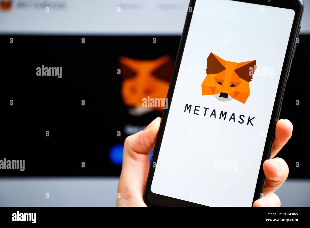 Ucraina, Odessa - Ottobre, 9 2021: Tenere la mano mobile con l'app MetaMask in esecuzione sullo schermo dello smartphone con il sito web metamask.io in background. MetaMask Foto Stock