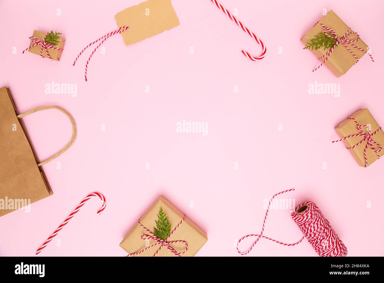 Natale, Capodanno sfondo accogliente. Scatole regalo artigianali fatte a mano con archi rossi, sacchetto di carta, caramelle, nastro rosso, biglietto da visita su sfondo rosa pastello. Foto Stock