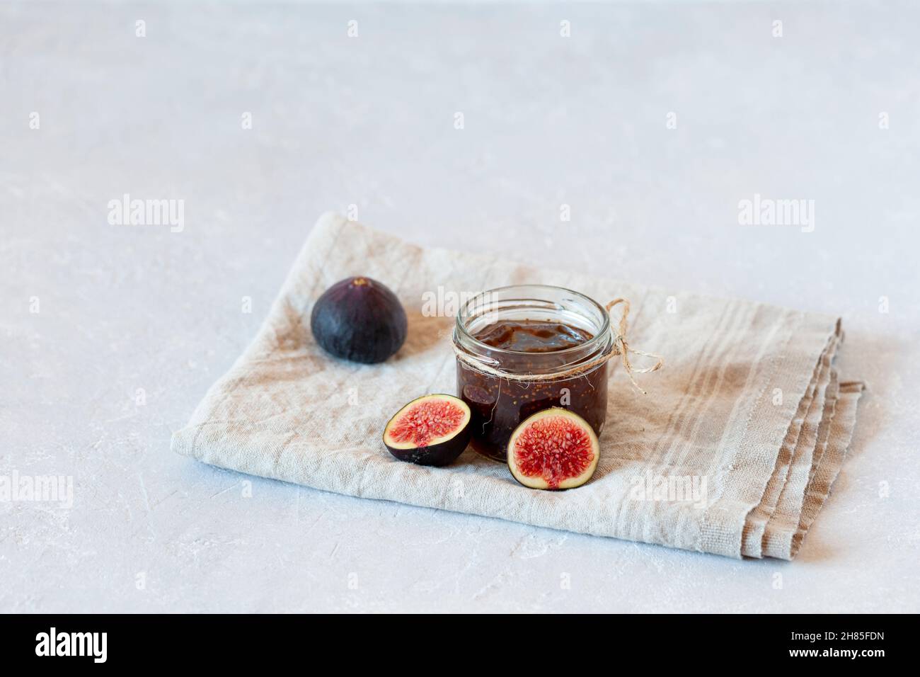 confit fico biologico fatto in casa da ricetta di famiglia in un piccolo vaso su sfondo grigio calcestruzzo, vista laterale, spazio copia Foto Stock