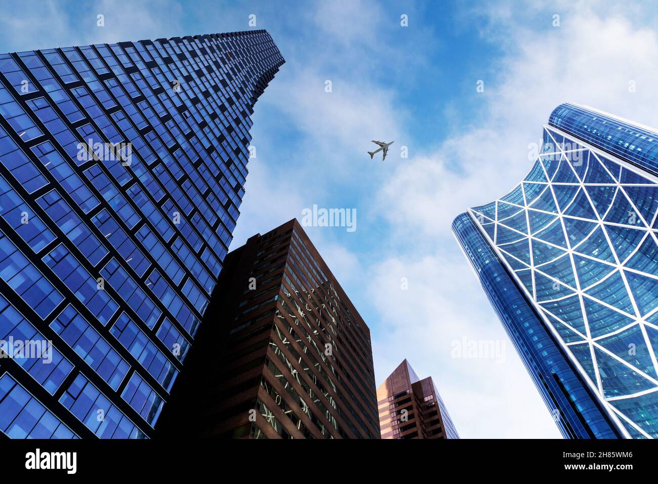 Vista dal basso di alti edifici di uffici nel quartiere degli affari del centro di Calgary, contro un cielo blu e nuvoloso con l'aereo in testa. Foto Stock