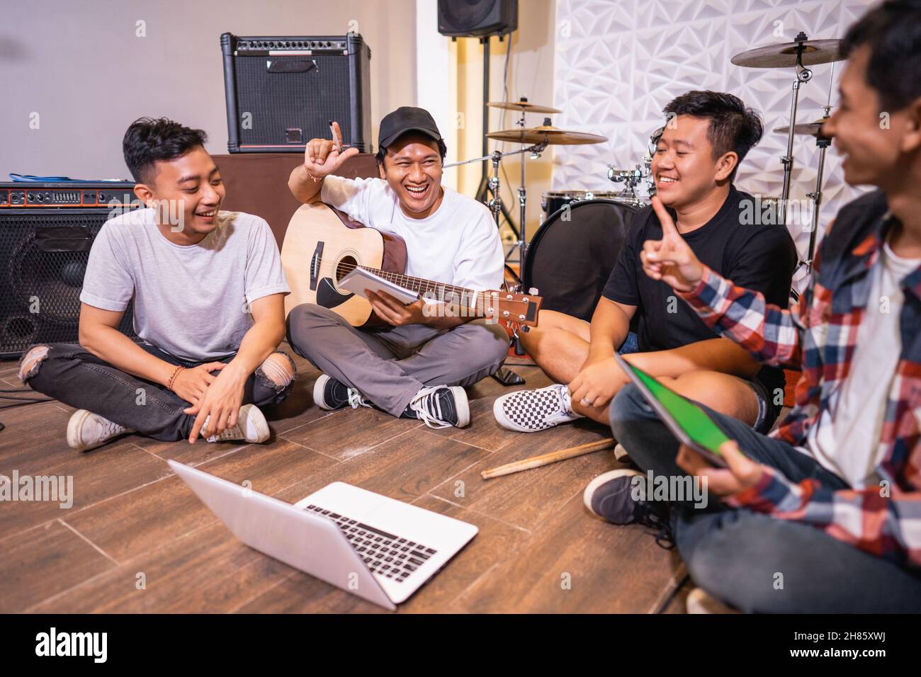 quattro persone che suonano chitarra e usano un computer portatile per guardare video clip di canzoni Foto Stock