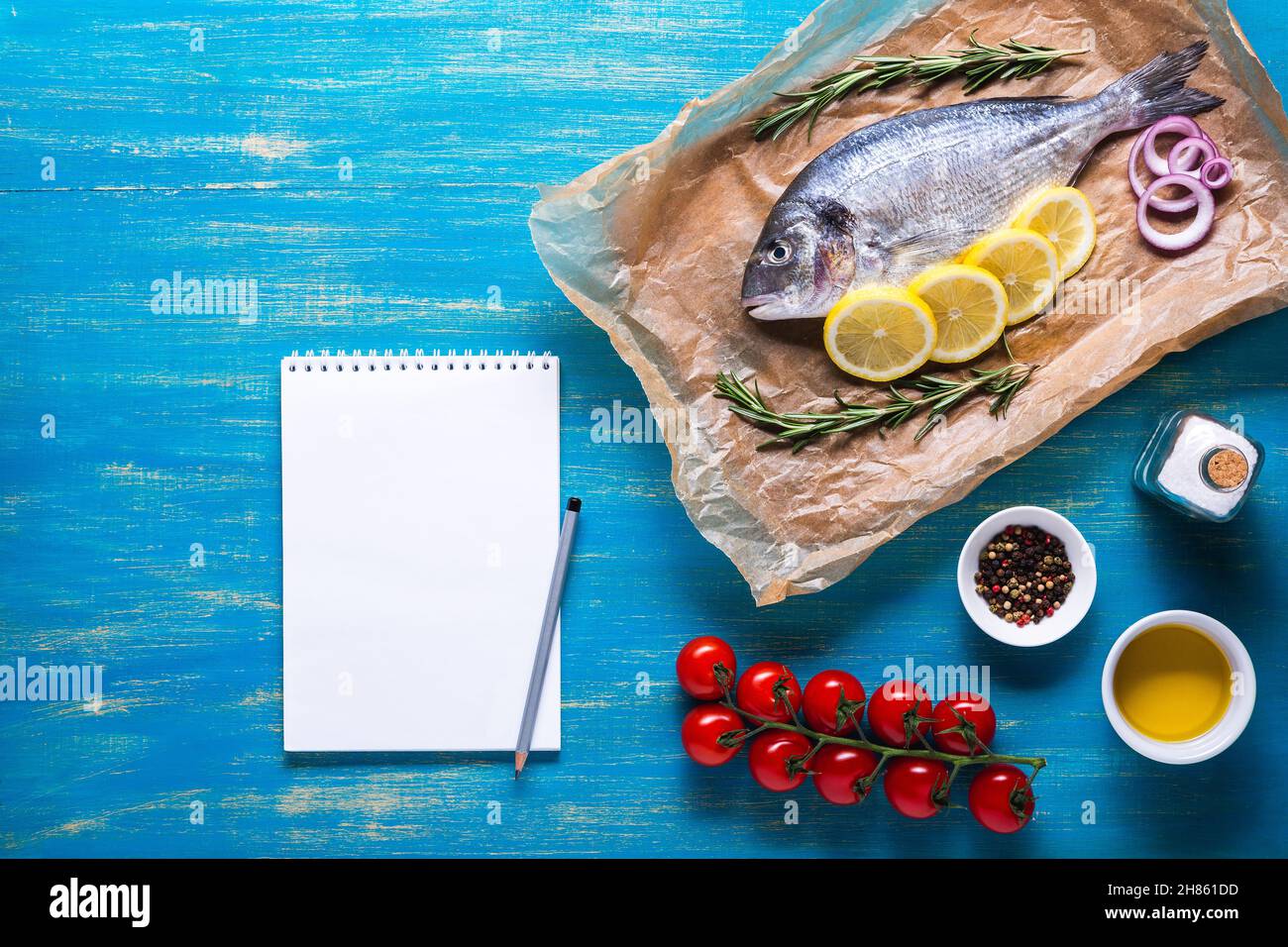 Pesce Dorado su carta da cucina con spezie e un taccuino per ricetta o menu. Vista dall'alto su sfondo blu. Foto Stock