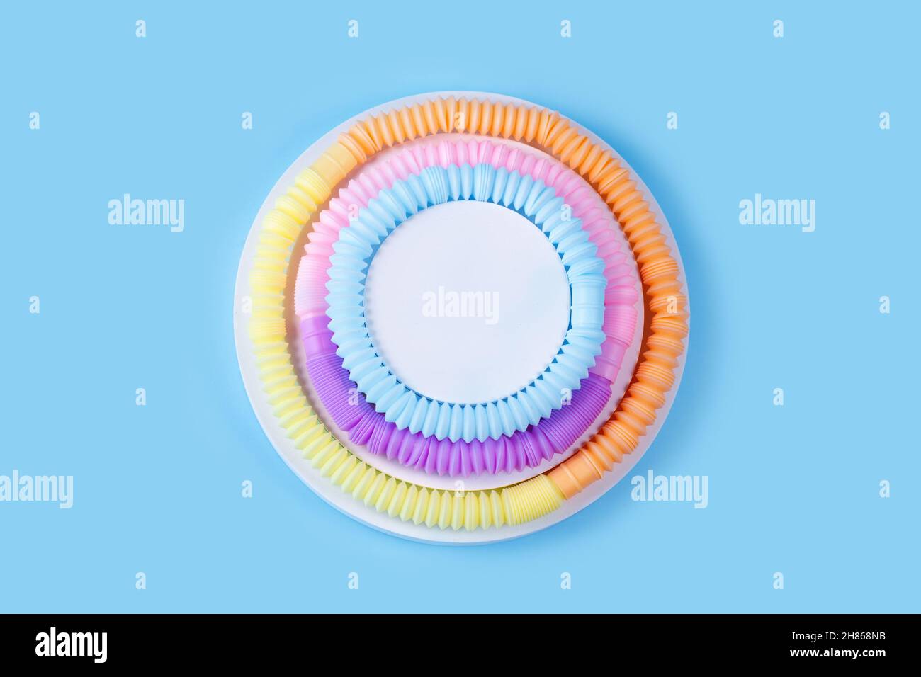 Tubi pop cerchio composizione sotto forma di una torta su sfondo blu. Collezione di poptubes sensoriali Trendy 2021. Giocattoli antistress popolari per bambini. Foto Stock