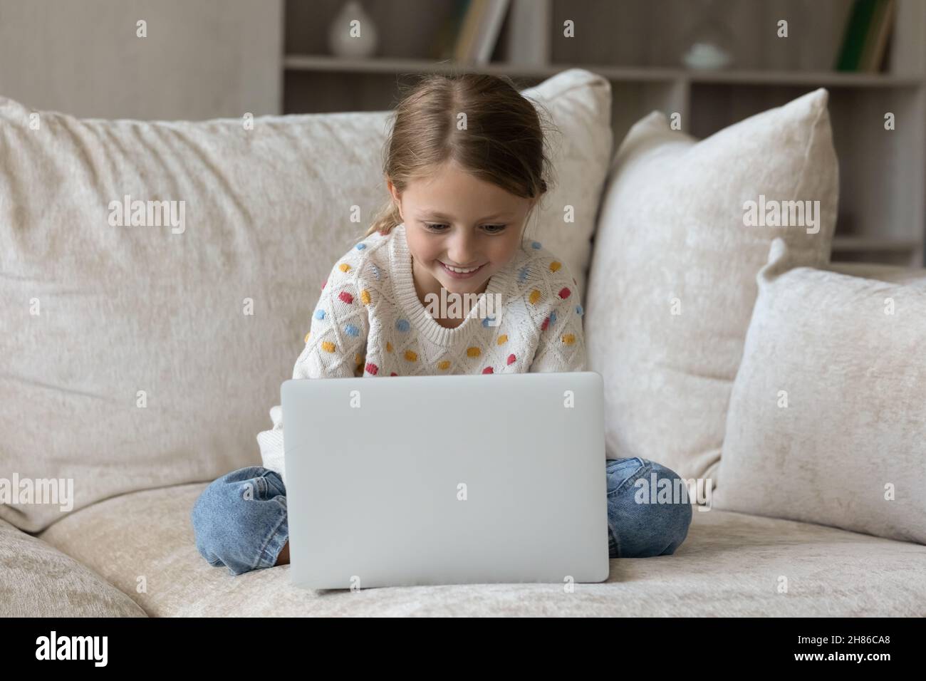 Gioiosa piccola ragazza carina bambino usando il computer, seduto sul divano. Foto Stock