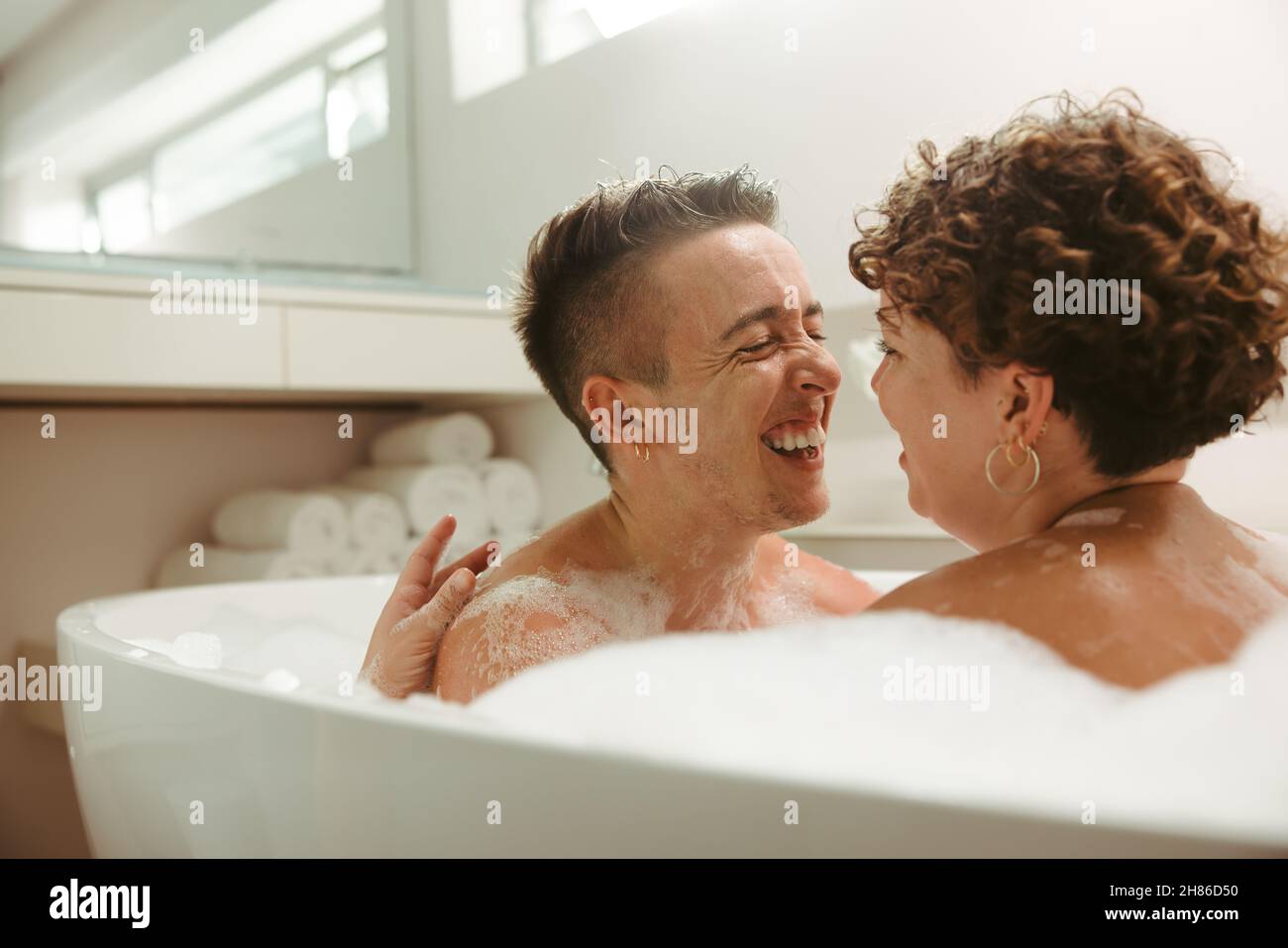 Spensierate giovani coppie queer che hanno un bagno romantico bolla a casa. Felice coppia giovane divertirsi insieme nella vasca da bagno. Spesa giovane coppia LGBTQ+ Foto Stock