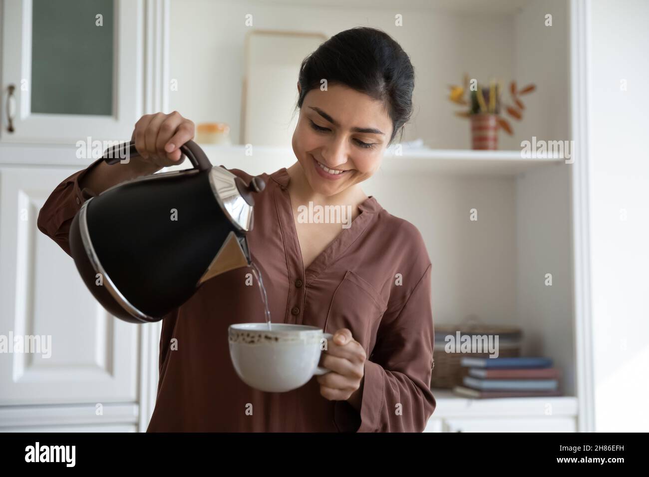 Sorridente giovane etnia indiana donna versando acqua calda in tazza. Foto Stock