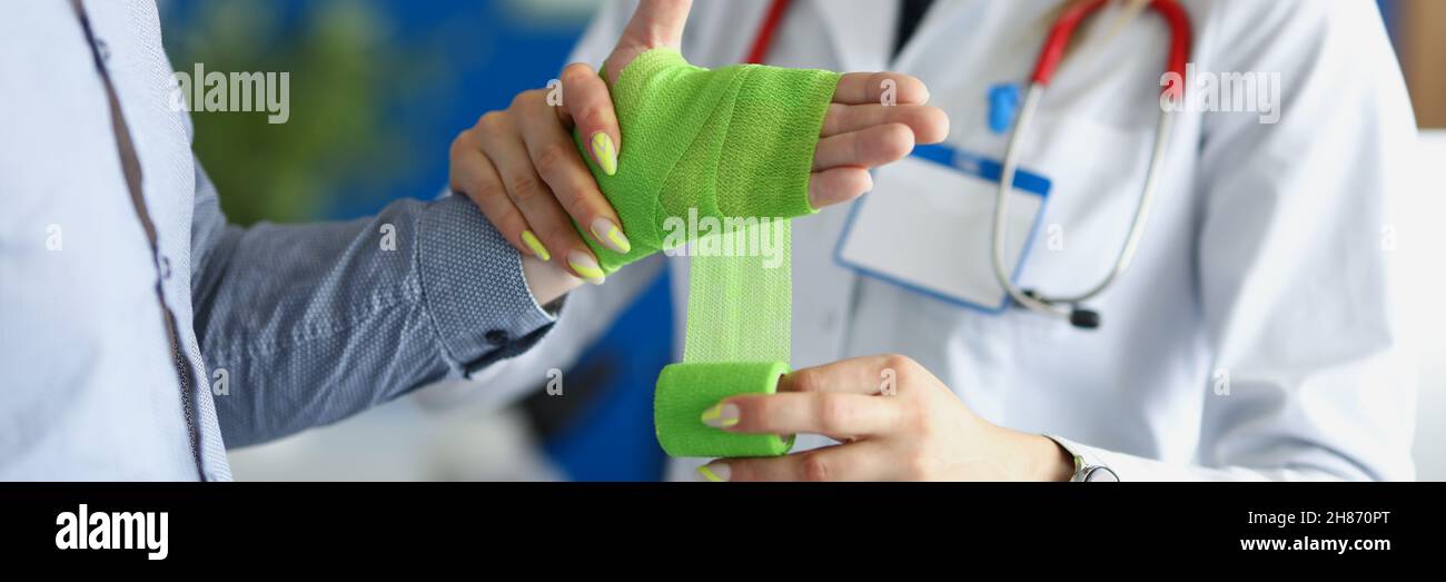 Medico bendaggio della ferita sul braccio del paziente con bendaggio verde nel closeup clinico Foto Stock