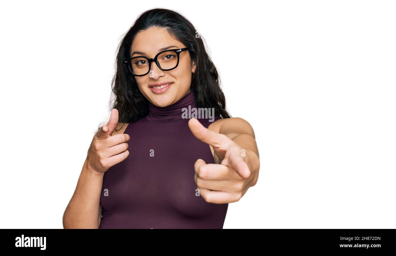 Bruna giovane donna che indossa abiti casual e occhiali puntando le dita alla macchina fotografica con volto felice e divertente. Buona energia e vibrazioni. Foto Stock