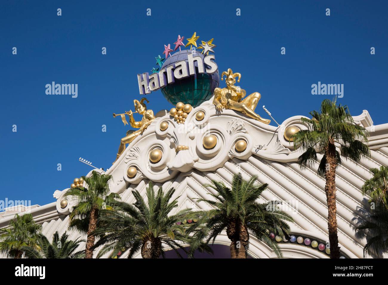 Las Vegas, Nevada, Stati Uniti. Ornamento di carnevale dorato che adorna la facciata superiore dell'Harrah's Las Vegas Hotel and Casino, palme in primo piano. Foto Stock