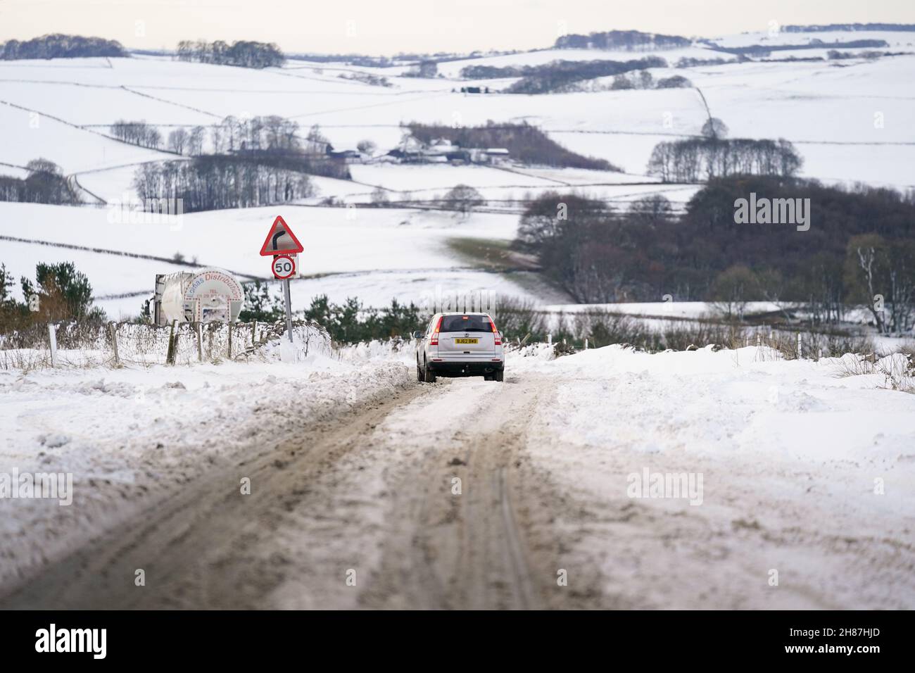 I veicoli tentano di viaggiare lungo la A515 innevata nei pressi di Biggin, nel Peak District, Derbyshire, in mezzo a condizioni di gelo all'indomani di Storm Arwen. Data foto: Domenica 28 novembre 2021. Foto Stock