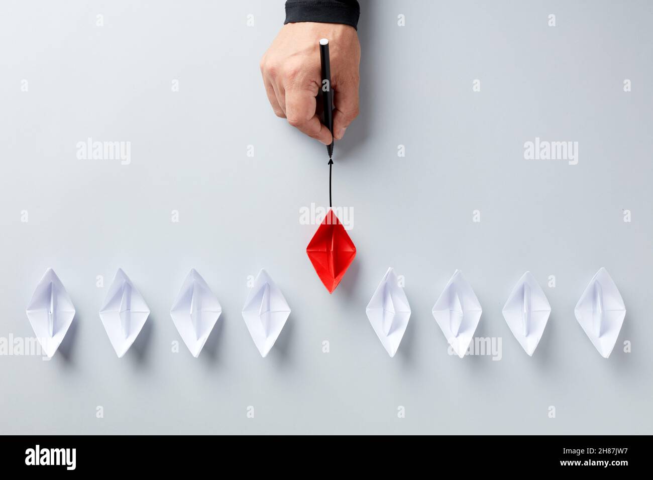 Guida alla startup aziendale, vantaggio competitivo, consulenza o concetto di leadership. La mano maschile mostra la direzione verso la barca di carta rossa che risalta fr Foto Stock