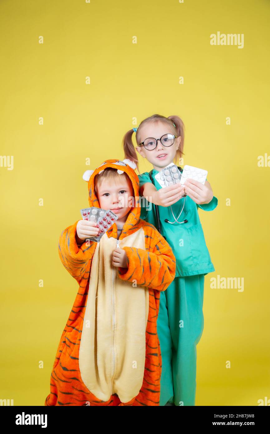 I bambini giocano a un medico, una ragazza vestita da medico e un ragazzo vestito da tigre tiene le vesciche con le pillole nelle loro mani Foto Stock