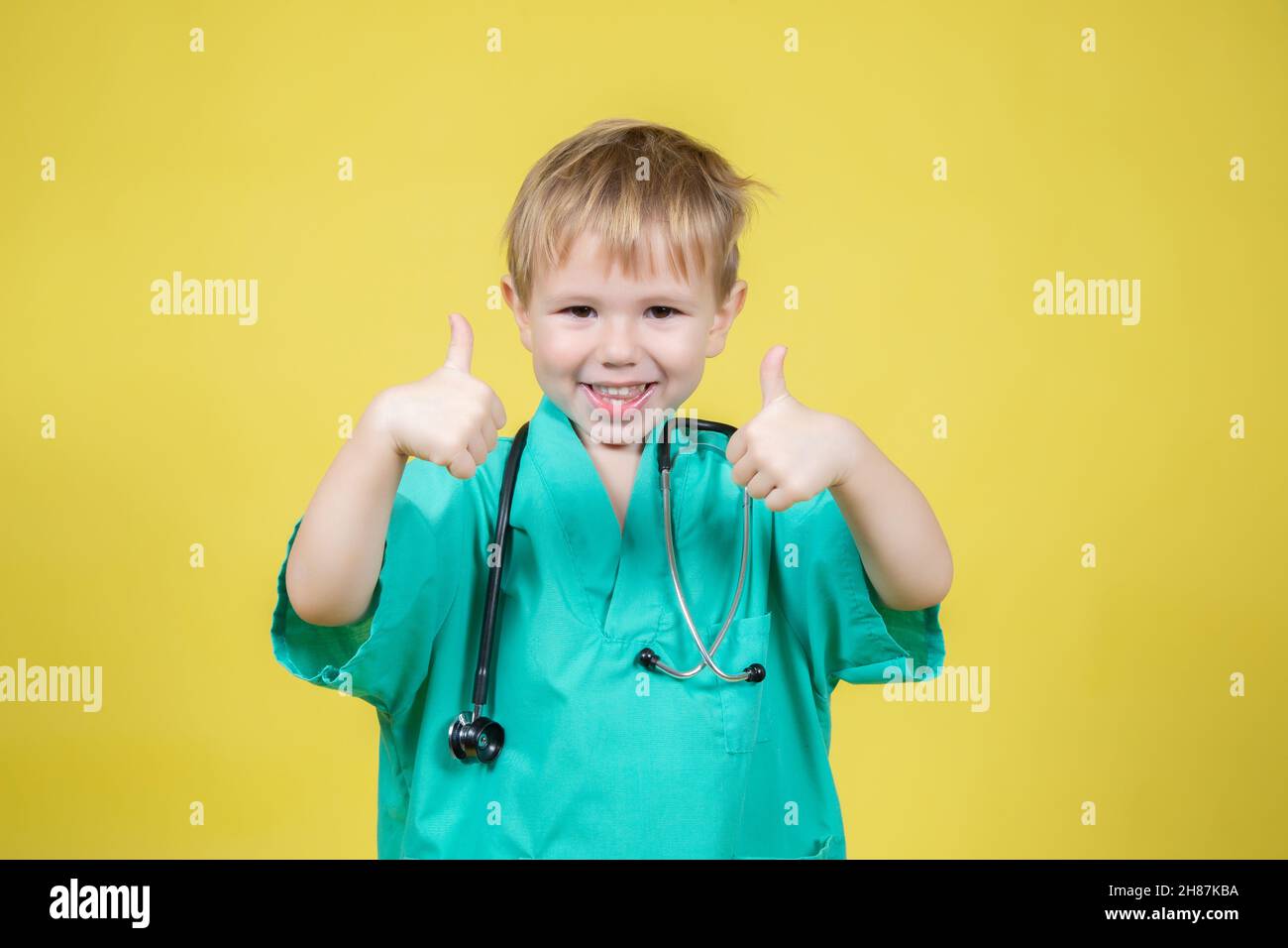 Ritratto di carino ragazzo caucasico vestito di medici verde mostrando pollice su gesto su sfondo giallo Foto Stock