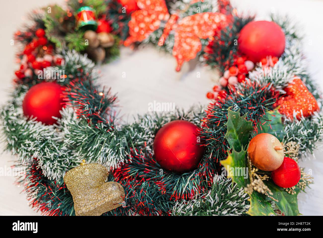 Corona di Natale di tinsel decorativo, bacche rosse di Natale e Natale albero festivo giocattoli sulla porta anteriore primo piano. Corona fatta a mano per la casa decorati Foto Stock