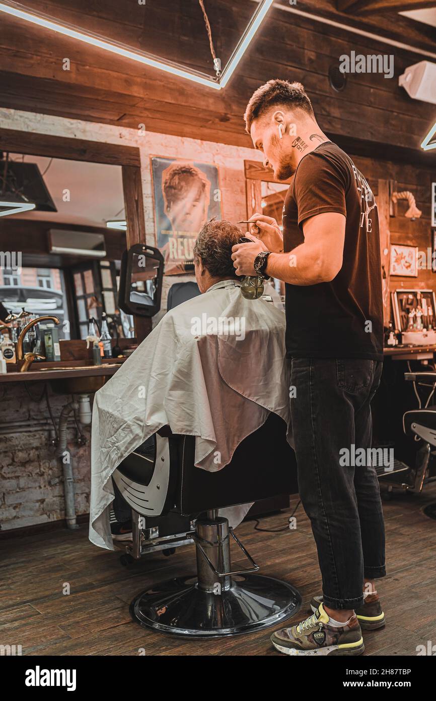 Barbiere. Parrucchiere esegue professionalmente un taglio per capelli per gli uomini. Uomo cliente siede in sedia professionale del barbiere e parrucchiere fa i capelli. Foto Stock