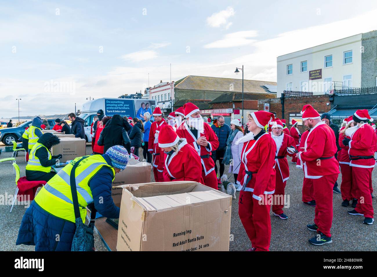 Le file di persone, tutte vestite da Padre Natale, si accingono a registrarsi per un posto nella 'Sana's on the Bay' benefica corsa in aiuto dei pellegrini ospizi sul lungomare a Herne Bay in Kent in una mattinata amaramente fredda a fine novembre. Foto Stock