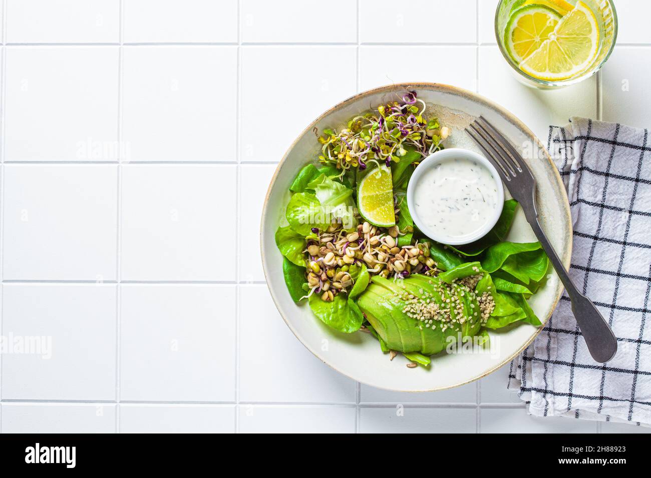 Insalata di disintossicazione verde con avocado, germogli, semi di canapa e condimento yogurt, sfondo piastrellato bianco, vista dall'alto, spazio copia. Foto Stock Insalata di disintossicazione verde con avocado, germogli, semi di canapa e condimento yogurt, sfondo piastrellato bianco, vista dall'alto, spazio copia. Foto Stock