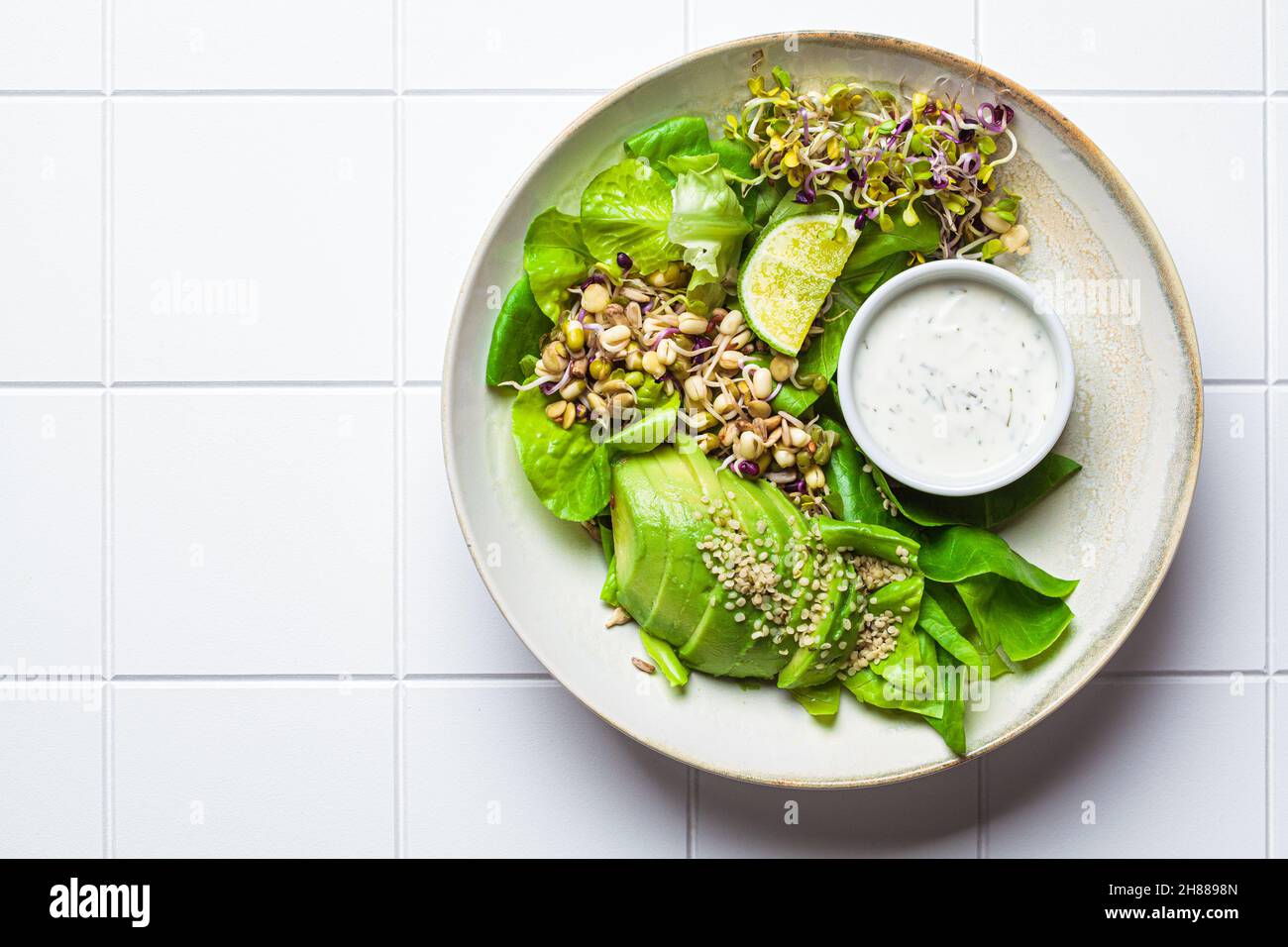 Insalata di disintossicazione verde con avocado, germogli, semi di canapa e condimento yogurt, sfondo piastrellato bianco, vista dall'alto, spazio copia. Foto Stock Insalata di disintossicazione verde con avocado, germogli, semi di canapa e condimento yogurt, sfondo piastrellato bianco, vista dall'alto, spazio copia. Foto Stock