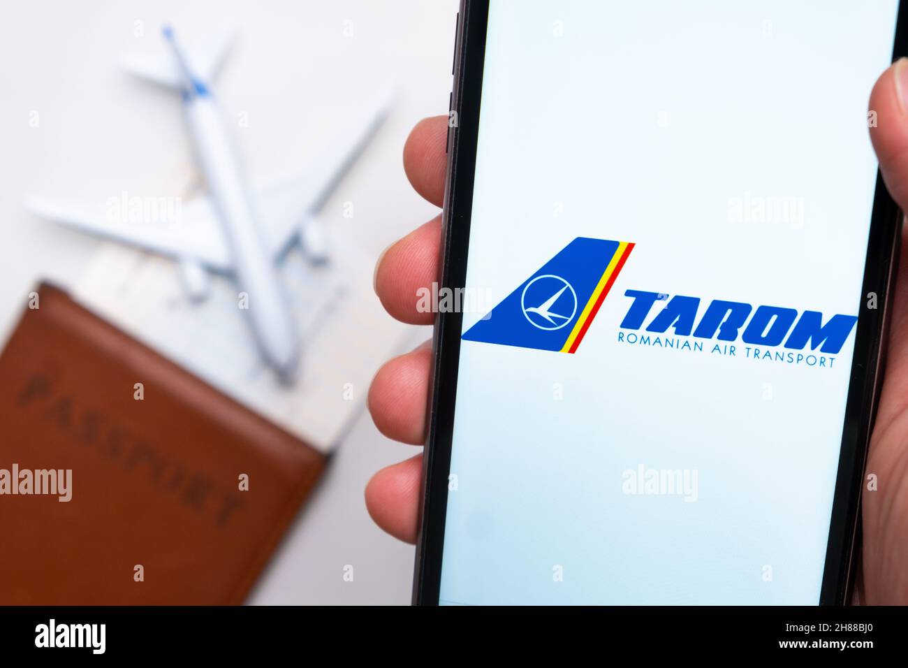 App Tarom Romanian Air Transport Airlines sullo schermo del telefono cellulare in mano con aereo, carta d'imbarco e passaporto sullo sfondo. Il concetto dell'applicazione mobile delle compagnie aeree. Novembre 2021, San Francisco, USA Foto Stock