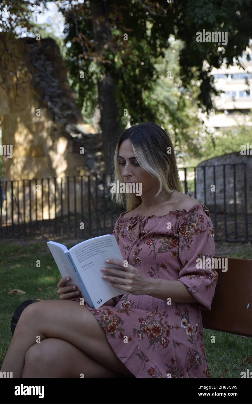 donna che legge un libro in un parco durante la giornata di sole guardando la macchina fotografica, guardando un libro, seduto su una panca, durante un inverno, giorno d'estate Foto Stock