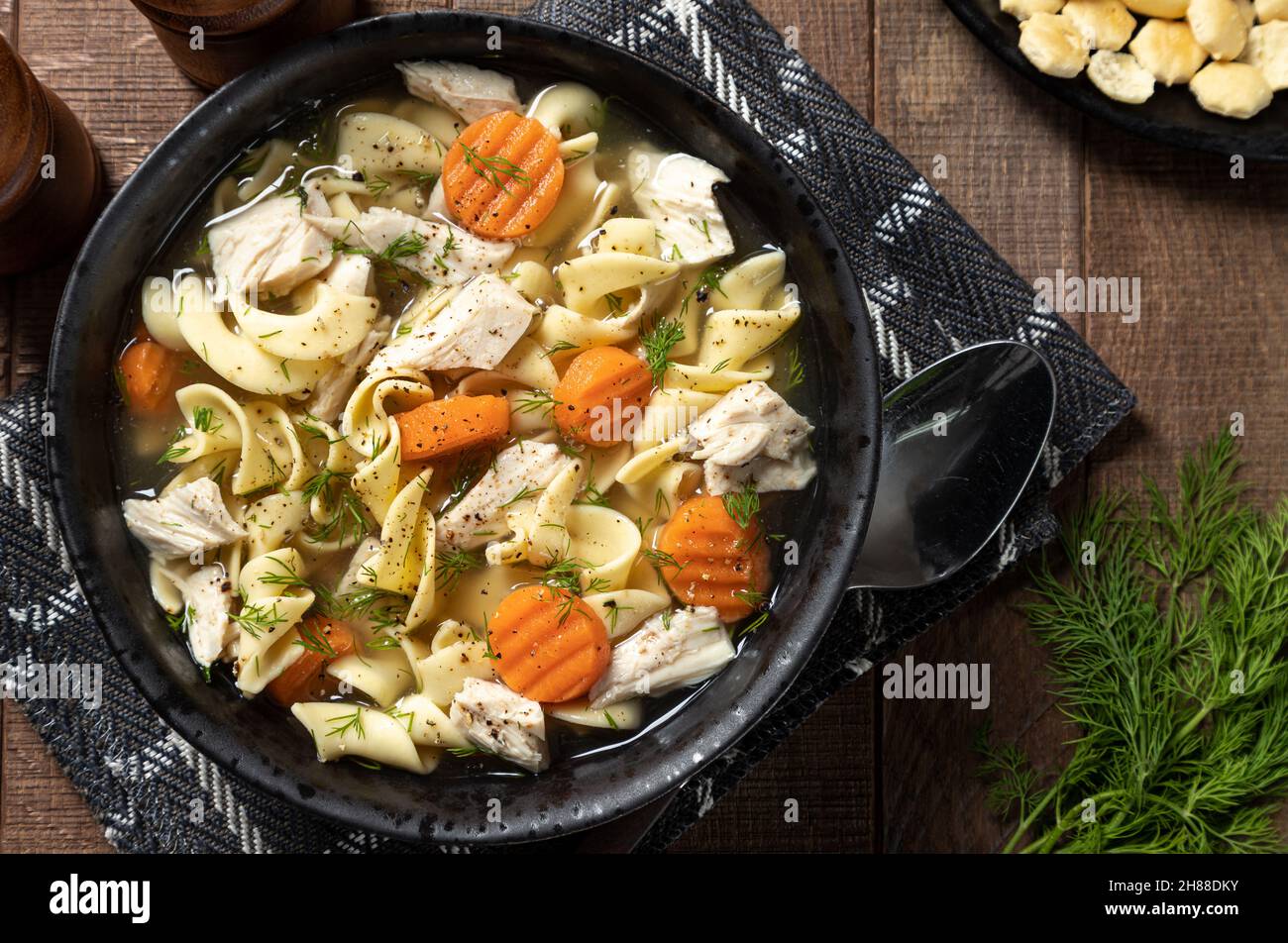 Vista dall'alto di una ciotola di zuppa di spaghetti di pollo con carote e aneto su un tavolo di legno Foto Stock