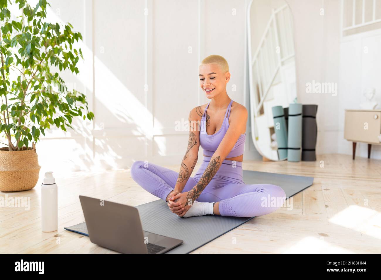 Yoga online. Fit signora che pratica la meditazione con il computer portatile, seduto sul tappeto fitness in posizione lotus di fronte al computer Foto Stock