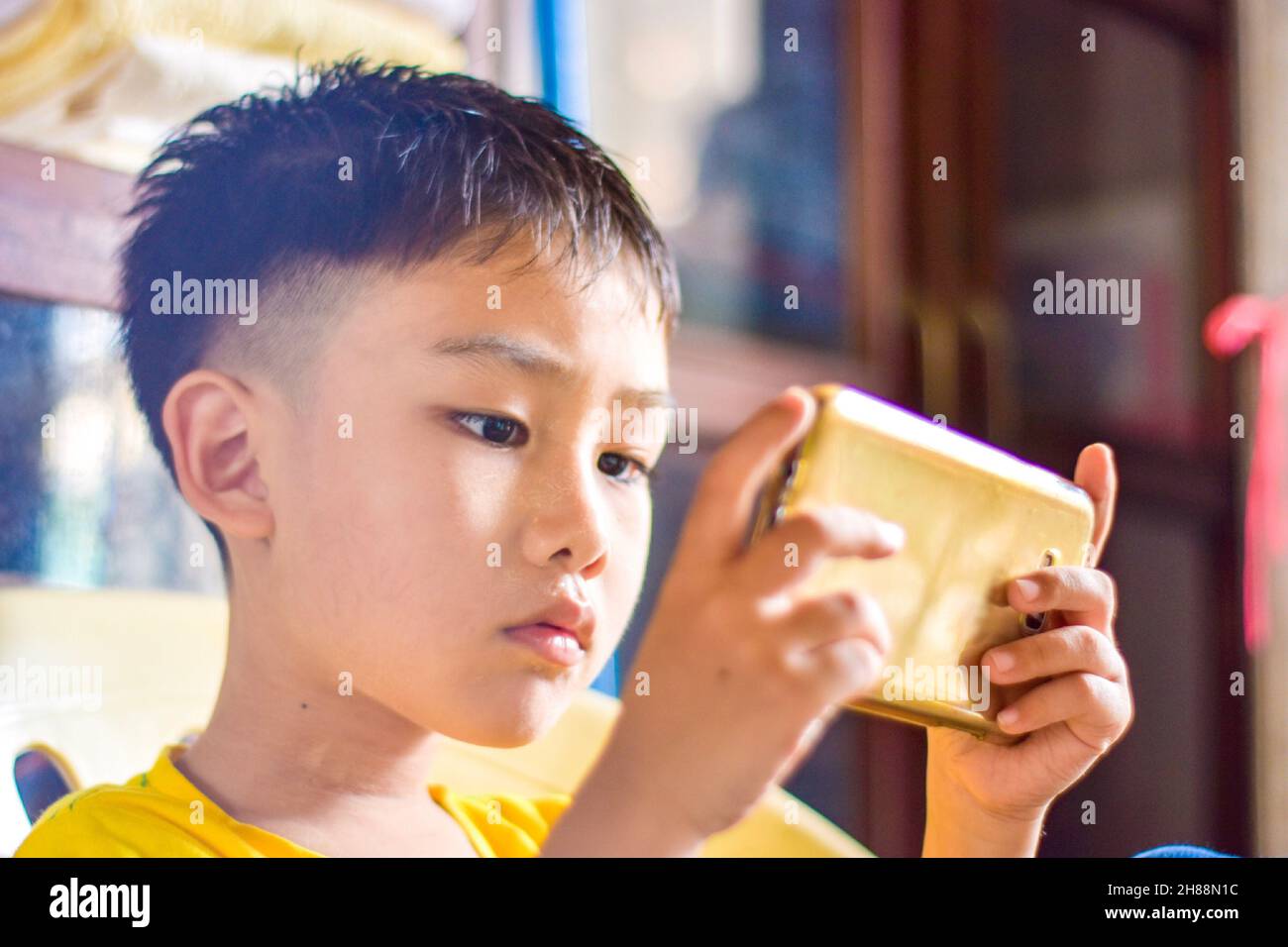 Bambino asiatico con gli occhi squadrati giocare a gioco mobile con smartphone. Concetto di affaticamento degli occhi, dipendenza dallo schermo e tempo di visualizzazione eccessivo. Foto Stock
