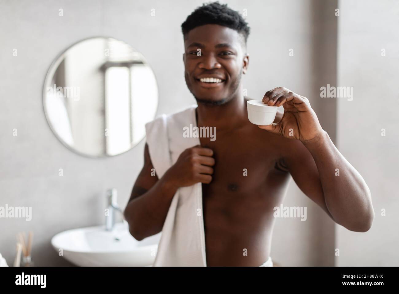 African American Male che mostra vaso crema viso posa in bagno Foto Stock