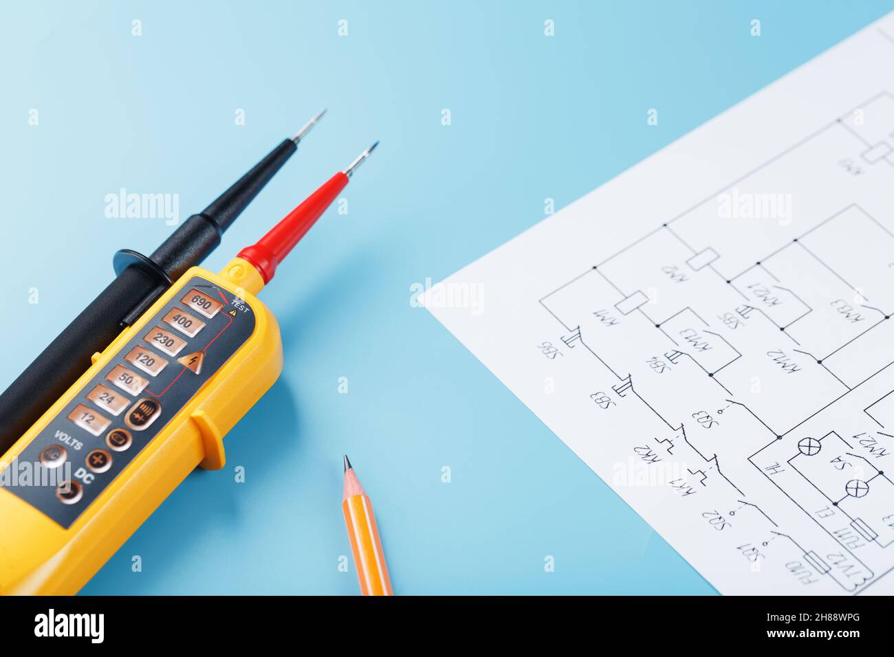 Indicatore di tensione giallo con uno schema elettrico su sfondo blu. Test e verifica delle reti elettriche Foto Stock