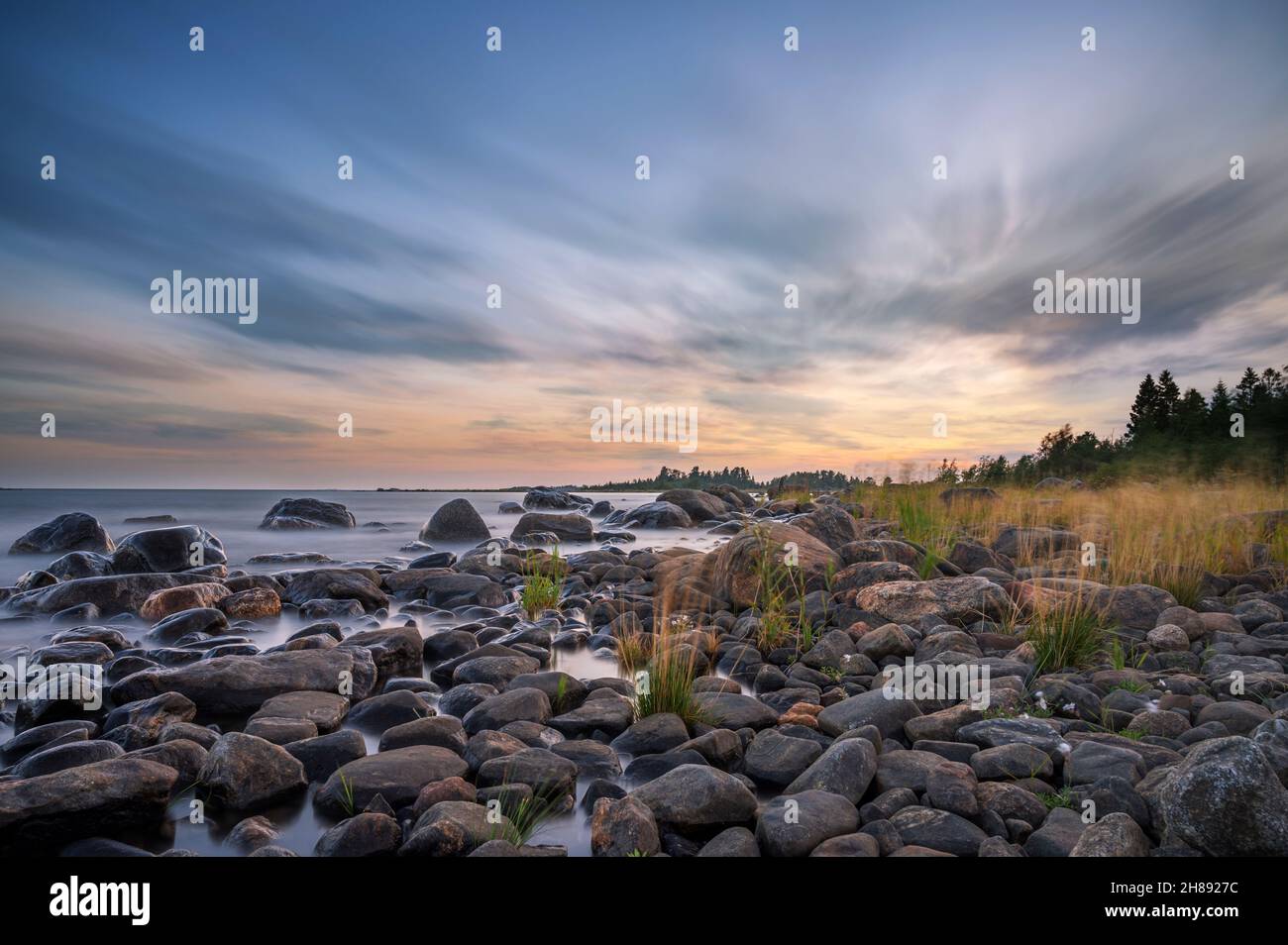 Lunga esposizione di un magnifico tramonto morbido e colorato vicino alla pietra del mare. Bel movimento nube con pietre di mare. Foto Stock
