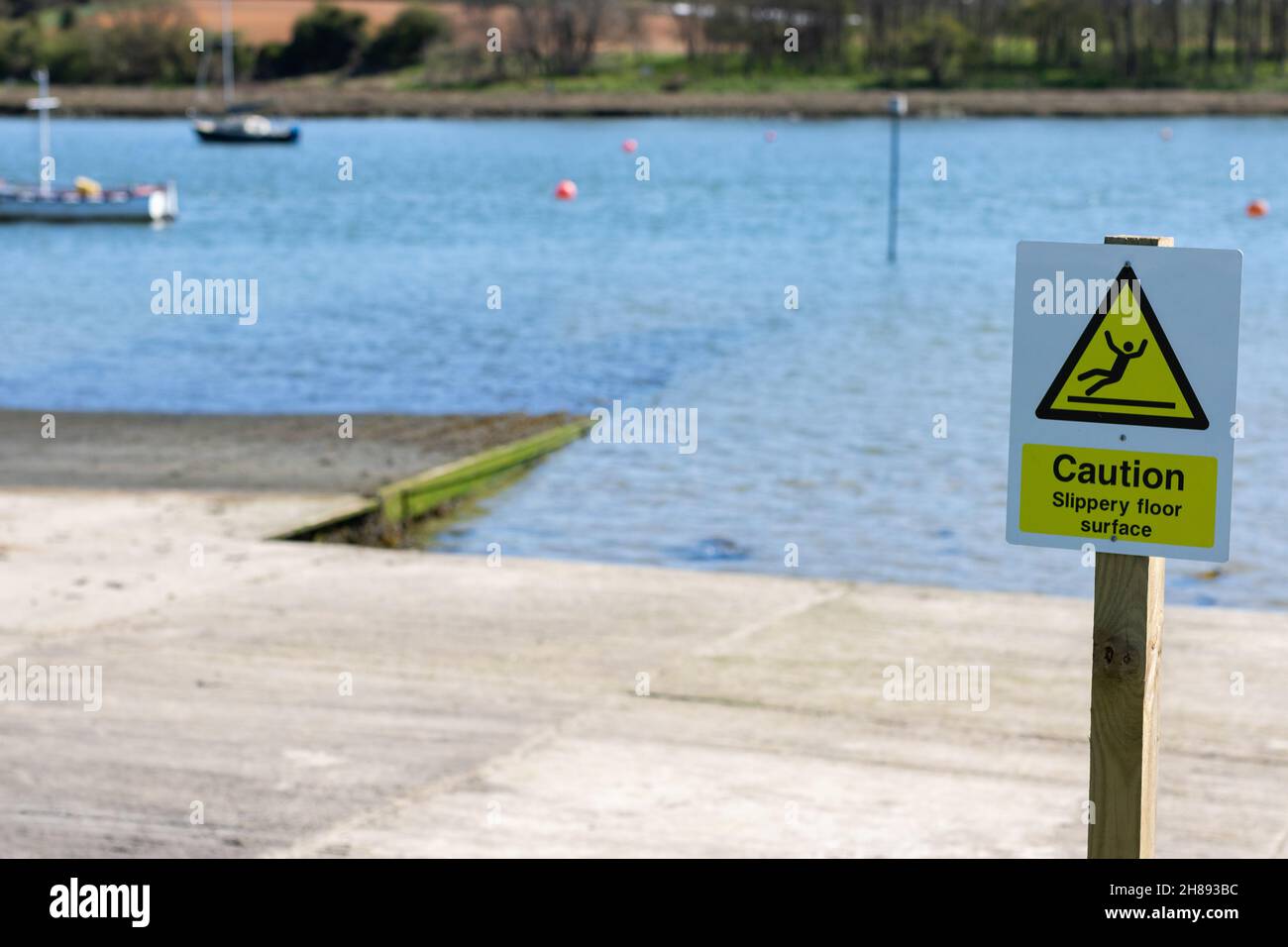 Cartello segnaletico per pavimento scivoloso su un molo vicino a un fiume. Il segno bianco e giallo ha anche chiaro simbolo di uomo scivola e cadere sulla parte superiore. Foto Stock