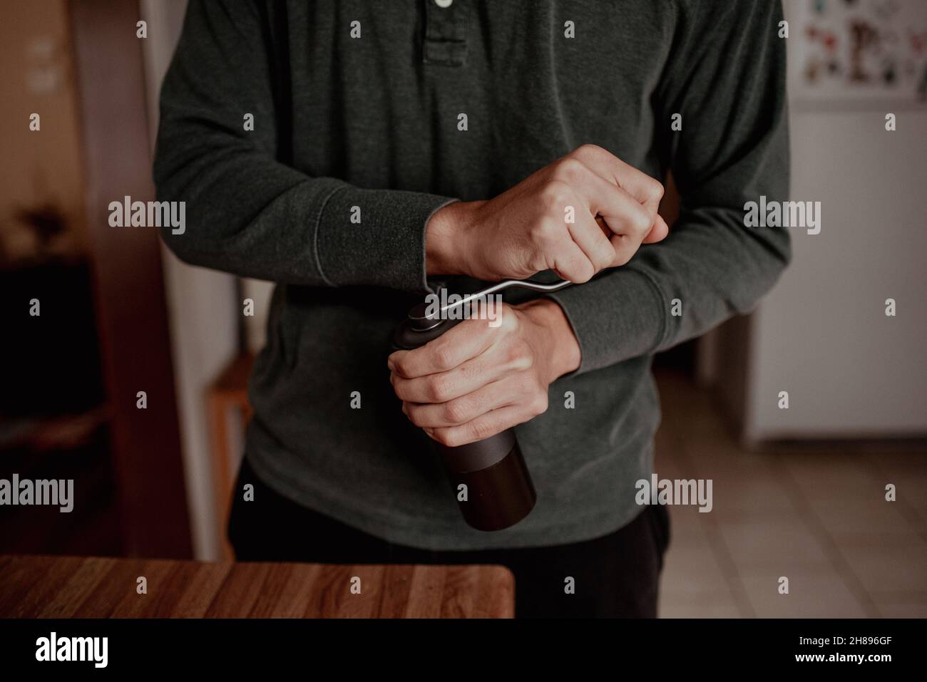 Giovane uomo di macinazione hipster di corsa mista con piccolo macinacaffè manuale in cucina a casa con illuminazione soffusa. Foto Stock