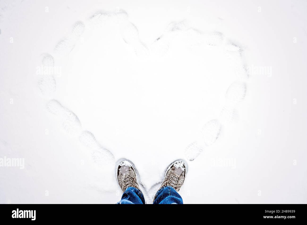 Ciao inverno, stagione invernale, San Valentino, amore romantico. Vista dall'alto dell'impronta degli scarponi da trekking nella neve fresca. Due piedi in stivali e disegnato cuore in Foto Stock