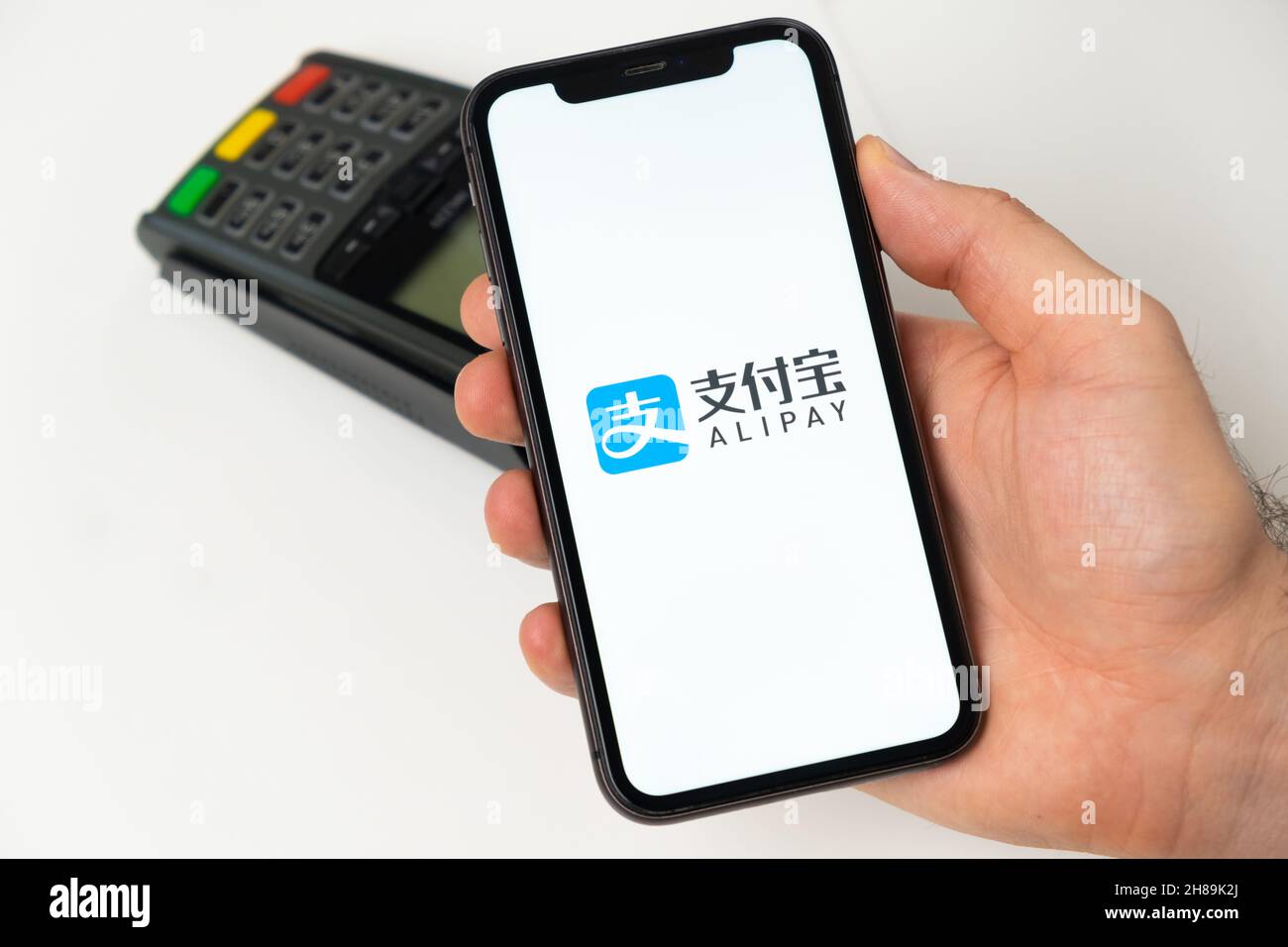 Pagamento Alipay per acquisti online con terminale di pagamento POS wireless in background. Uomo in possesso di un telefono cellulare con app per il pagamento. Novembre 2021, San Francisco, USA Foto Stock